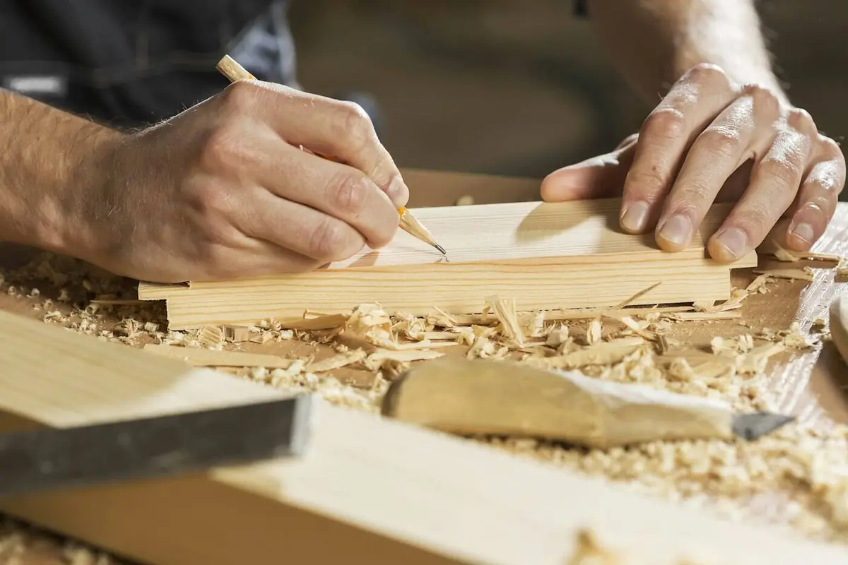 Hands marking a pine board with a pencil among wood shavings